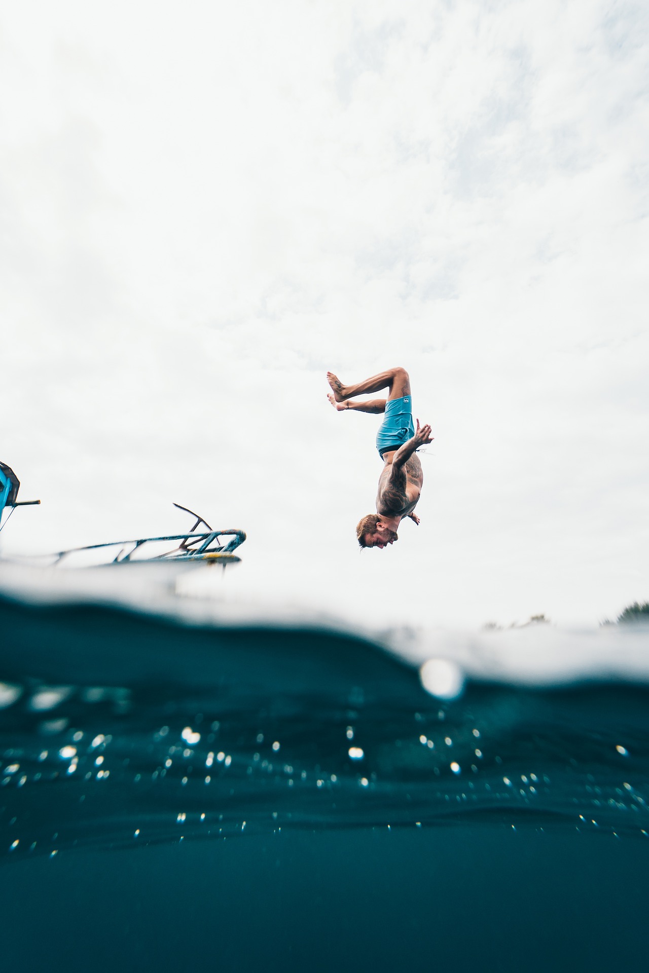 Man doing a back somersault off a yacht into the ocean. Man is shown upside down legs bent up to the sky and face down looking to the ocean. Foreground shows camera is half in the ocean so bottom third of image is below the water line. Signifies the freedom and bliss one can enjoy when they have financial independence and retire early.